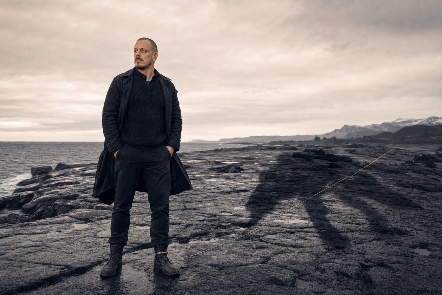 Mikkel Krogsholm på en nordisk kyst med en enorm ulveskygge bundet af en tynd metallisk tråd.